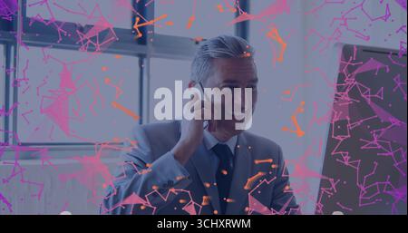 Talking man in suit viewing monitor and using smartphone at desk by window, with network graphics Stock Photo
