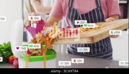Home cook in striped apron pushing peelings into kitchen juicer at home, with social media icons Stock Photo