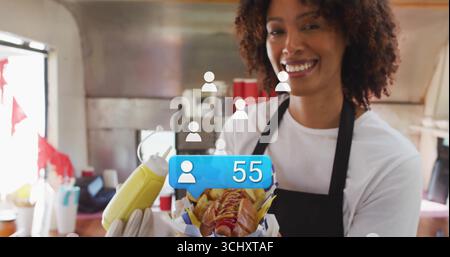 Serving server in apron offering hot dog with fries, mustard bottle in truck kitchen, copy space Stock Photo