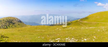 Wide view of the Creueta plateau in the Pyrenees with grassy hills, rocky terrain, and distant mountain layers under a clear summer sky. Stock Photo