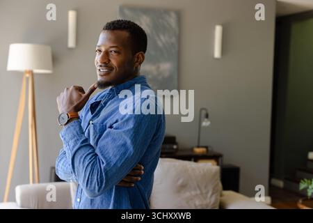 Smiling confidently, man in denim shirt sitting thoughtfully at home Stock Photo