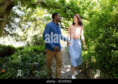 Happy Diverse couple walking hand in hand through lush garden, enjoying nature together Stock Photo