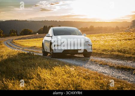White car on a gravel road through a golden meadow at sunset, Tesla Model Y Juniper, electric car Stock Photo