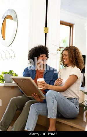 Young diverse couple unpacking boxes, smiling and holding picture frame and coffee at home Stock Photo