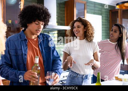 Diverse friends enjoying wine and conversation in modern kitchen, smiling and relaxed, at home Stock Photo