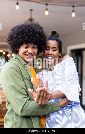 Joyful young Diverse couple celebrating engagement with excitement and laughter on patio Stock Photo