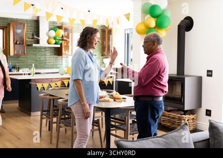 Celebrating birthday at home, senior diverse friends smiling and having conversation together Stock Photo