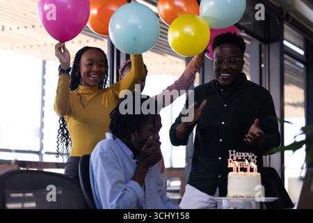 Celebrating birthday at office, African American colleagues with balloons and cake Stock Photo