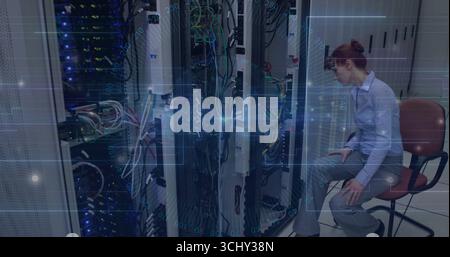 Network technician on rolling chair adjusting cables in server room with blinking racks, copy space Stock Photo
