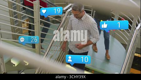 Walking staff in casual attire carrying laptop on metal staircase in atrium showing media overlays Stock Photo