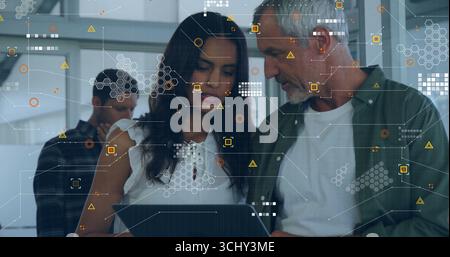 Collaborating colleagues wearing casual attire focusing on laptop at office with HUD overlays Stock Photo