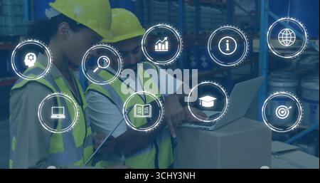 Warehouse workers in safety vests and hard hats updating stock in warehouse, with tablet and laptop Stock Photo
