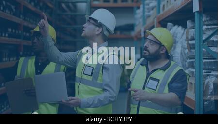 Reviewing workers wearing helmets checking stock in warehouse aisle, with laptop and clipboard Stock Photo