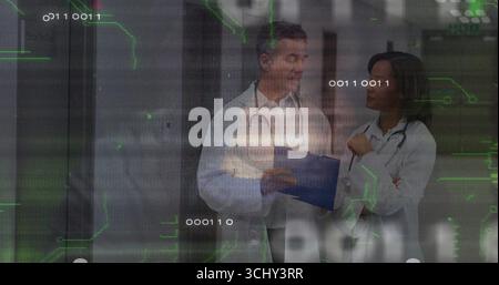 Standing two doctors consulting over blue clipboard in hospital corridor, with data overlay Stock Photo