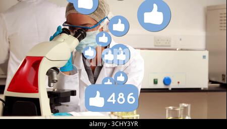 Observing scientist wearing coat examining microscope in lab, liquid test tubes and thumbs-up icons Stock Photo
