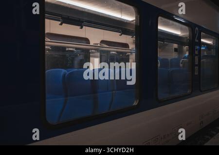 View through the train window showing empty blue seats in a second-class carriage at night in Serbia. Stock Photo