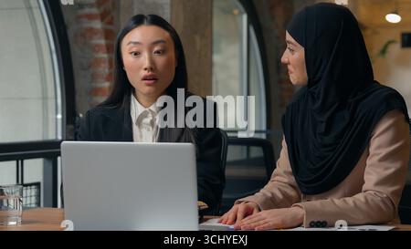 Two multiracial diversity business women co-workers employers multiethnic businesswomen girls Korean Asian Muslim females surprise talking video call Stock Photo