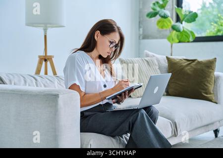 Middle aged serious woman working on c with laptop notepad Stock Photo