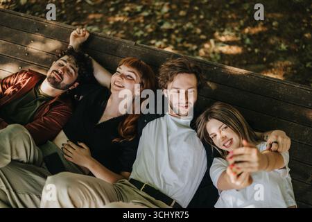 Four friends relax outdoors taking a selfie together on a summer day Stock Photo