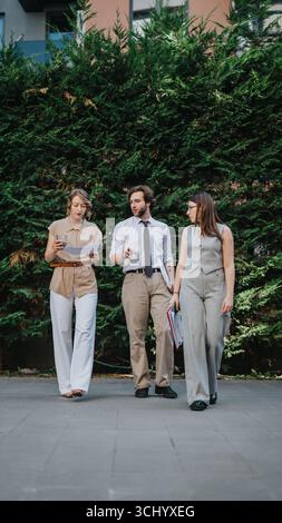 Three colleagues walking outdoors discussing business ideas confidently Stock Photo