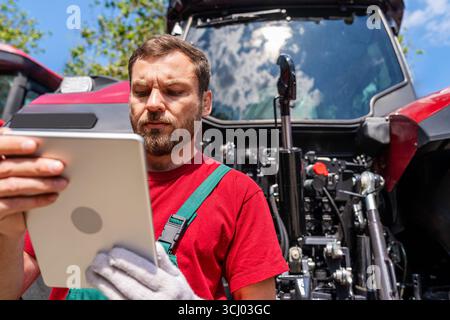 Man agricultural mechanic using digital tablet near tractor outdoors in countryside Stock Photo