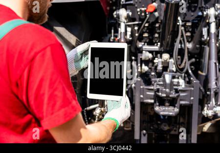Agricultural mechanic using digital tablet for wireless machinery diagnostics. Stock Photo