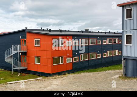 Modern Buildings With Spiral Staircase Longyearbyen Svalbard Norway / LONGYEARBYEN, Svalbard — Modern buildings featuring a prominent external spiral staircase rise in central Longyearbyen, one section painted vibrant orange and the main body a deep blue. The color contrast is characteristic of the town's architecture, where a color-coded scheme attributed to designer Grete Smedal assigns distinct hues to buildings by original function. Structures throughout Longyearbyen are typically raised on wooden stilts to prevent heat transfer to the permafrost below — which extends roughly 400 feet (122 Stock Photo