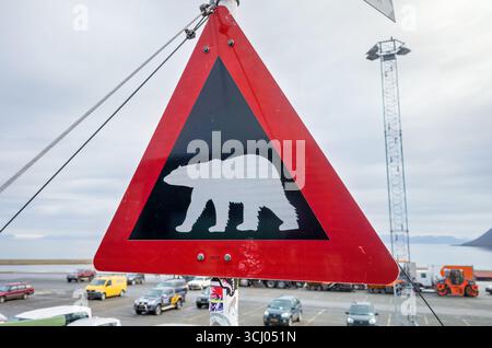 Polar Bear Warning Sign Longyearbyen Svalbard / LONGYEARBYEN, Svalbard — A triangular polar bear warning sign displaying a black silhouette of a polar bear against a white background, bordered by a red reflective triangle, is posted in Longyearbyen. Such signs are common throughout Svalbard, where the polar bear population is estimated to number around 3,000 across the archipelago. Norwegian authorities strongly encourage — and in practice require — anyone traveling outside the settlement perimeter to carry a rifle, as encounters with bears are a genuine risk. Longyearbyen is the administrativ Stock Photo