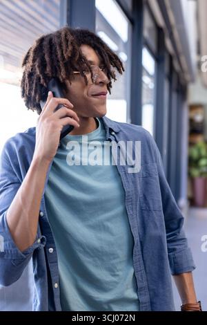 Young man in office talking on smartphone, looking confident and engaged Stock Photo