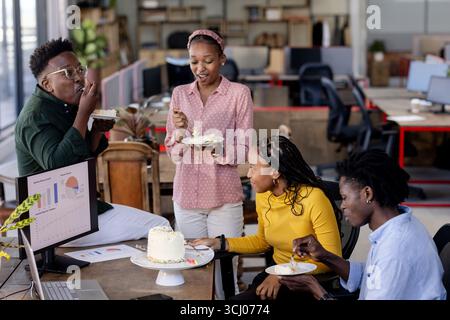 In office, African American colleagues having cake, smiling and socializing during break Stock Photo