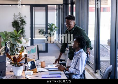 In office, colleagues discussing data on computer screen, collaborating and smiling Stock Photo