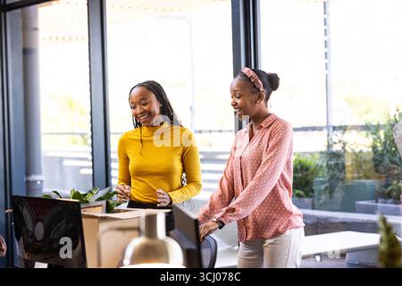 Two women collaborating in modern office, smiling and discussing creative project Stock Photo