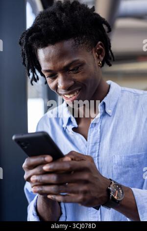 Smiling man using smartphone at office, engaging with digital content Stock Photo