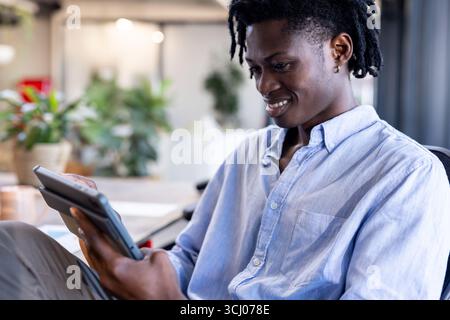 African American man using tablet in modern office, smiling and focused on work Stock Photo
