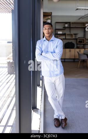 Confident businessman in blue shirt standing by office window, looking thoughtful Stock Photo