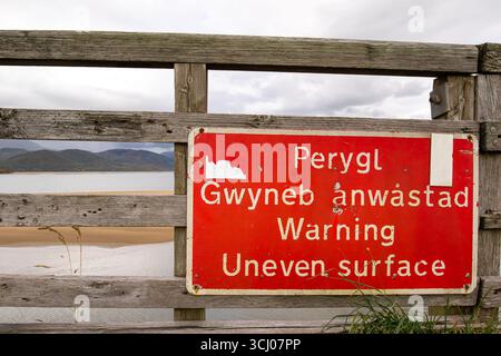 Barmouth Bridge sign warning users of UNEVEN SURFACE when crossing on this timber viaduct bridge over River Mawddach estuary in Wales. Stock Photo