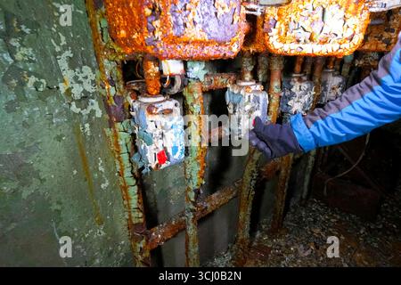 Pressing a button by hand on the control panel in an old abandoned bunker with peeling paint and damp walls. Stock Photo