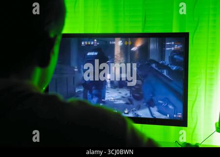 Gamer streamer playing shooter game at monitor, rear view from behind ...