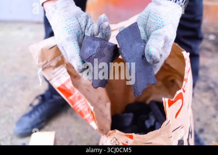 Man in gloves takes charcoal from a bag with coal Stock Photo