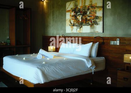 Sumberkima, Bali, Indonesia – August 27, 2025: Modern minimalist bedroom with white linens, wooden furniture, and wall decoration Stock Photo