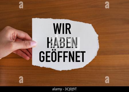 Wir haben geöffnet. We are open Wir haben geöffnet. We are open Woman hand holds a piece of paper with a note. Retail place, small business, store, info graphic, message, consumerisim, opening event. note GER2005 wir haben geoeffnet Stock Photo