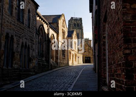 Late afternoon sunlight creates shadows on a deserted street with the tower of the ancient cathedral in the background, City of Durham, England. Stock Photo