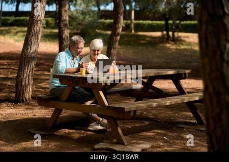 Senior couple using laptop and having breakfast in park Stock Photo