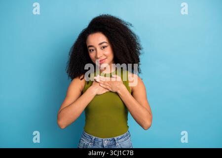 Young woman with curly hair holding hand to chest expressing gratitude and kindness on vibrant blue background Stock Photo
