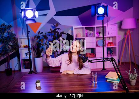 Popular blogger hosting a podcast with engaging visuals in a colorful studio featuring modern microphone equipment and neon lighting. Stock Photo