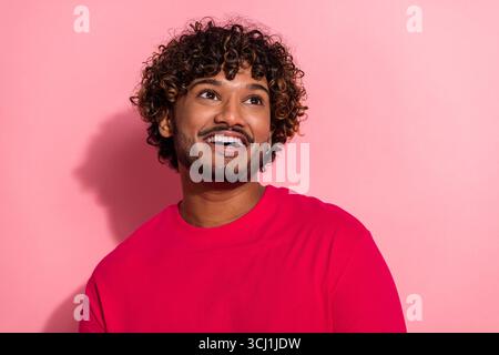 Young man in a red shirt with curly hair smiling joyfully while standing against a vibrant pink background Stock Photo