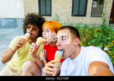 Three joyful friends enjoying ice cream cones and taking a selfie Stock Photo