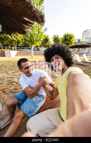 Two friends arm wrestling and taking a selfie in a park Stock Photo
