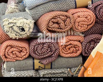 Rolled textiles with herringbone patterns in red, orange and gray stacked in a shop. Design, comfort and consumer choice represented through woven Stock Photo