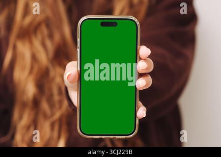 Smartphone with green screen. Blank mobile display held in hand. Technology gadget for mockup design. Digital communication background. Stock Photo